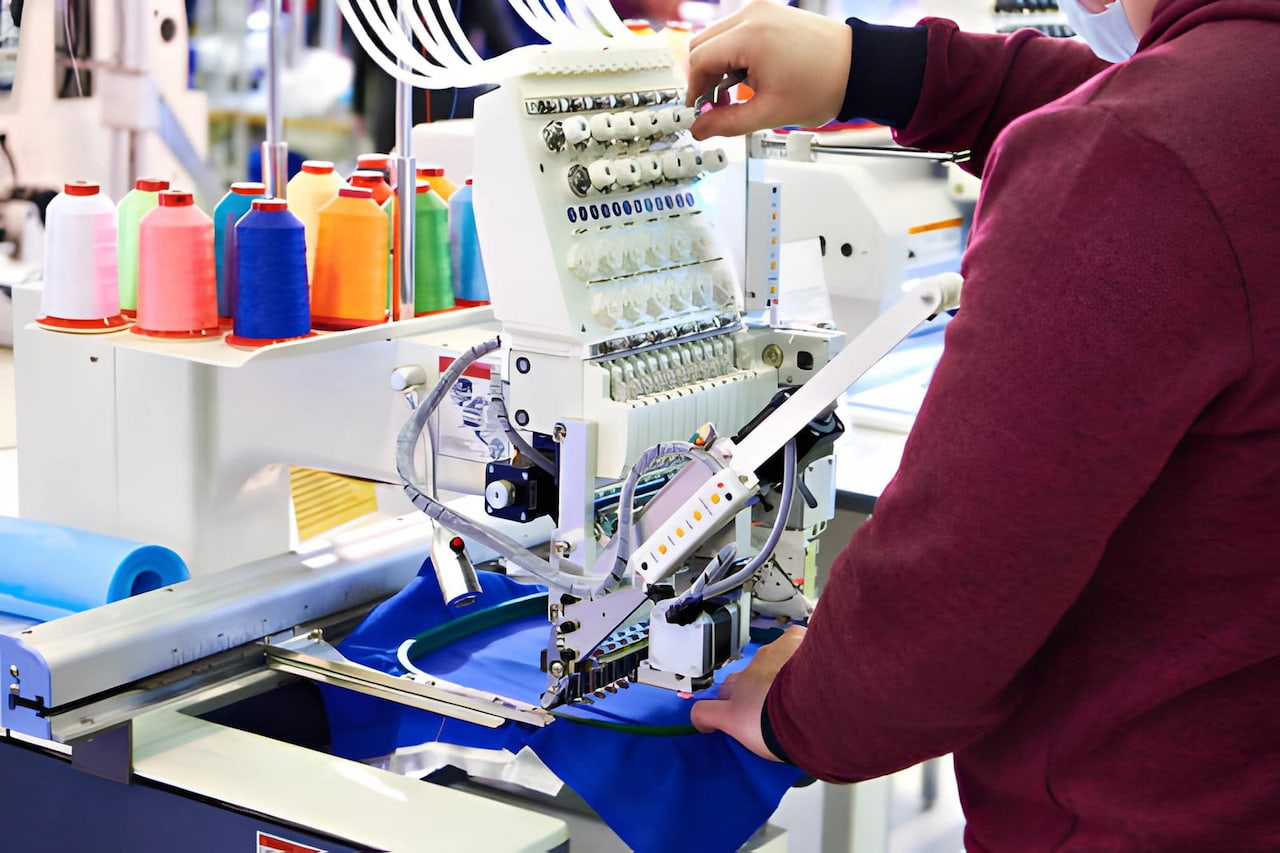 Machine de broderie textile en action avec fils colorés pour personnalisation de vêtements.